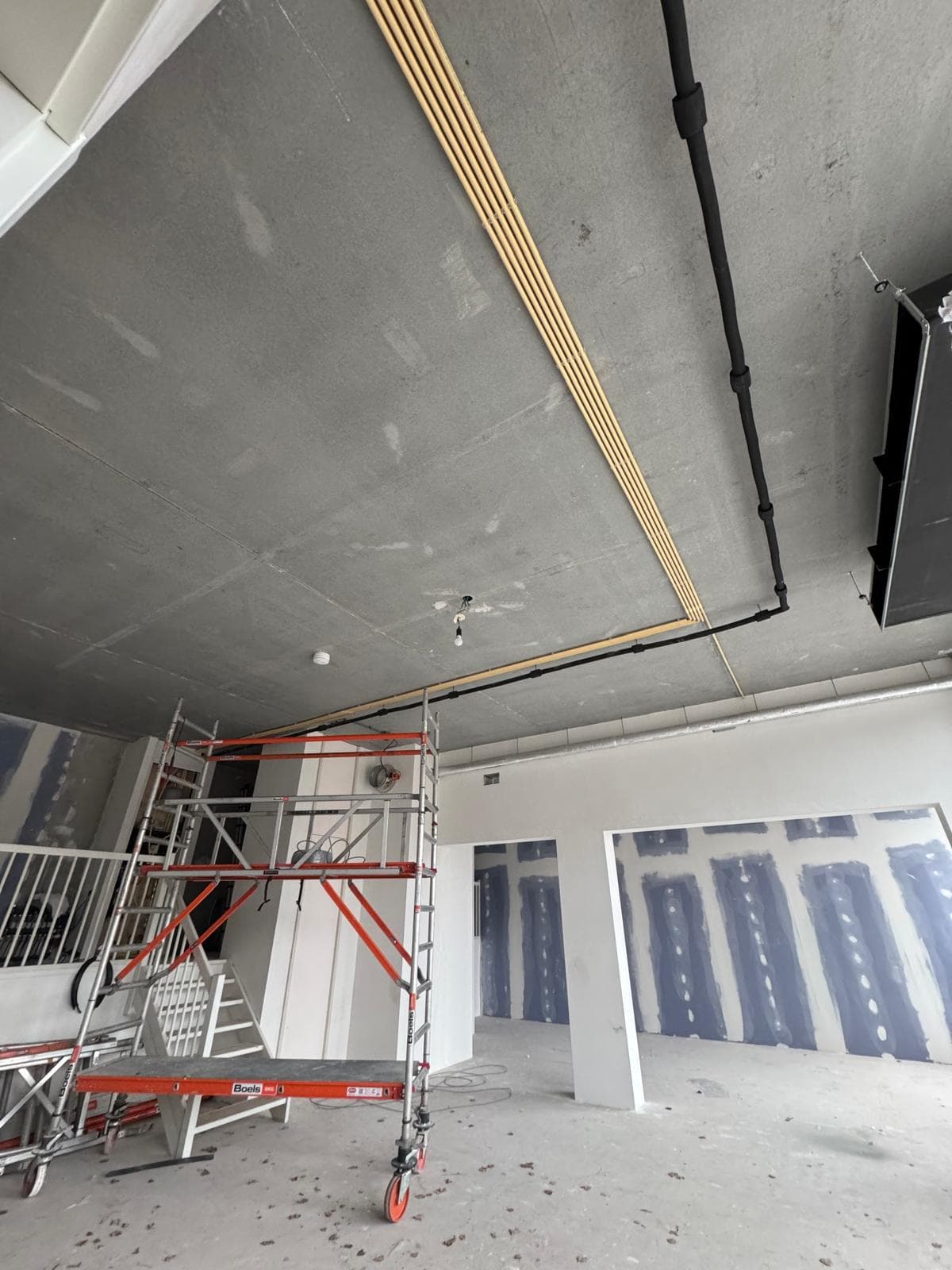 Metal scaffolding in an unfinished room with a concrete ceiling, exposed pipes, and drywall walls.